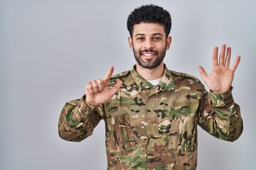 Sticker - Arab man wearing camouflage army uniform showing and pointing up with fingers number seven while smiling confident and happy.