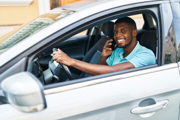 Wall Mural - Young african american man talking on the smartphone sitting on car at street