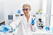 © Krakenimages.com - Middle age blonde woman working at scientist laboratory smiling looking to the camera showing fingers doing victory sign. number two.