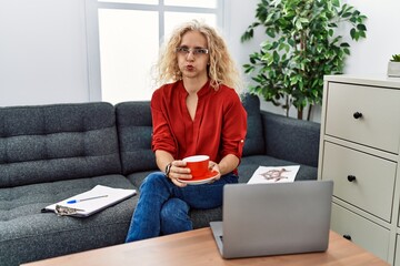 Canvas Print - Middle age psychologist woman at consultation office puffing cheeks with funny face. mouth inflated with air, catching air.