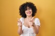 © Krakenimages.com - Young brunette woman with curly hair standing over yellow background pointing fingers to camera with happy and funny face. good energy and vibes.