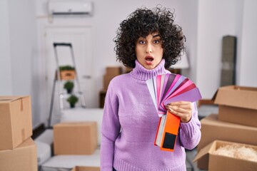 Poster - Young brunette woman with curly hair choosing color of new house wall scared and amazed with open mouth for surprise, disbelief face