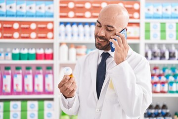 Sticker - Young bald man pharmacist holding pills bottle talking on smartphone at pharmacy