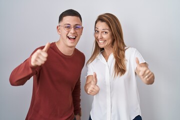 Sticker - Mother and son standing together over isolated background approving doing positive gesture with hand, thumbs up smiling and happy for success. winner gesture.