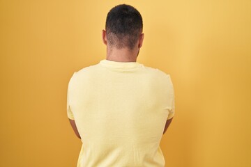 Poster - Young hispanic man standing over yellow background standing backwards looking away with crossed arms