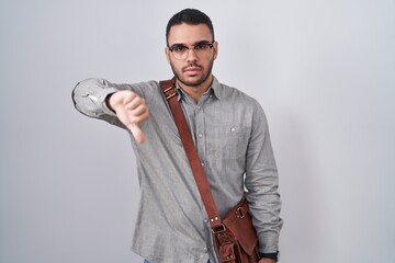 Wall Mural - Young hispanic man wearing suitcase looking unhappy and angry showing rejection and negative with thumbs down gesture. bad expression.