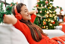 Young Latin Woman Listening To Music Sitting By Christmas Tree At Home
