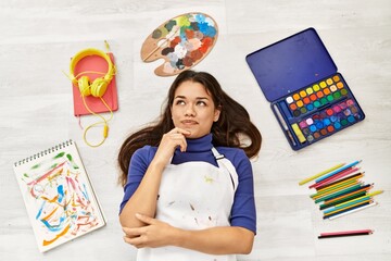 Sticker - Young brunette woman lying on the floor at art studio around artist things serious face thinking about question with hand on chin, thoughtful about confusing idea