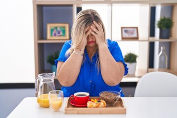 Poster - Caucasian plus size woman eating breakfast at home with sad expression covering face with hands while crying. depression concept.