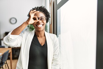 Wall Mural - African business woman working at the office smiling happy doing ok sign with hand on eye looking through fingers