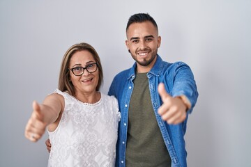 Sticker - Hispanic mother and son standing together approving doing positive gesture with hand, thumbs up smiling and happy for success. winner gesture.