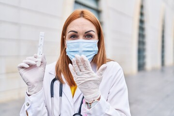 Sticker - Young doctor woman holding coronavirus infection test covering mouth with hand, shocked and afraid for mistake. surprised expression