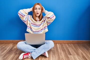 Sticker - Young woman using laptop at home sitting on the floor crazy and scared with hands on head, afraid and surprised of shock with open mouth