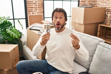 Canvas Print - Handsome middle age man holding led lightbulb and incandescent bulb afraid and shocked with surprise and amazed expression, fear and excited face.