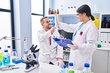 Wall Mural - Man and woman wearing scientists uniform high five with hands raised up at laboratory