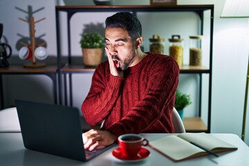 Canvas Print - Young hispanic man with beard using computer laptop at night at home afraid and shocked, surprise and amazed expression with hands on face