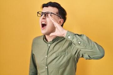 Poster - Non binary person standing over yellow background shouting and screaming loud to side with hand on mouth. communication concept.