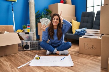 Sticker - Young brunette woman sitting on the floor at new home holding money stressed and frustrated with hand on head, surprised and angry face