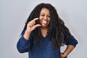 Sticker - Plus size hispanic woman standing over white background smiling and confident gesturing with hand doing small size sign with fingers looking and the camera. measure concept.