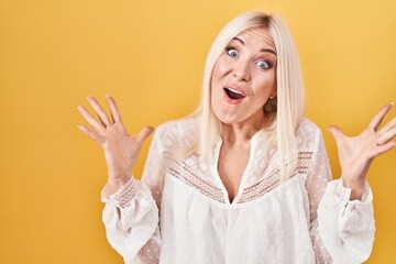 Poster - Caucasian woman standing over yellow background celebrating victory with happy smile and winner expression with raised hands