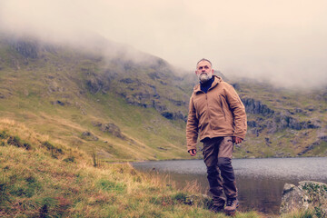 Wall Mural - Bearded Man reaching the destination  alone to  the lake in  mountains on foggy autumn day  Travel  Lifestyle concept The national park Lake District in England