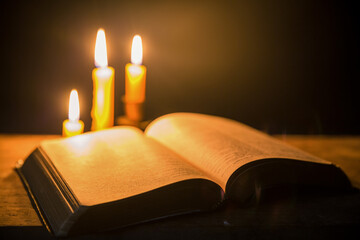 Wall Mural - Light candle with holy bible and cross or crucifix on old wooden background in church.Candlelight and open book on vintage wood table christianity study and reading in home.Concept of christ religion