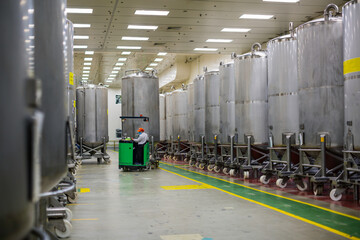 A male worker moving a bucket stainless vertical steel tanks equipment tank chemical cellar with scrolling wheel stainless steel tanks cleaning and treatment at shampoo