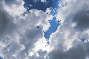 Wall Mural - The passenger airplane is flying far away in the blue sky and clouds. Dramatic clouds with the sun shining through them. Aircraft in the air. International passenger air transportation