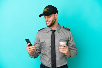 Poster - Young security man isolated on blue background holding coffee to take away and a mobile