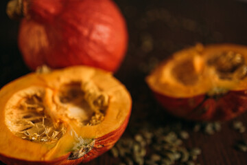 two halves of a pumpkin and one whole pumpkin in close-up on a table strewn with seeds