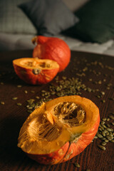 two halves of a pumpkin and one whole pumpkin in close-up on a table strewn with seeds. on the background of a sofa