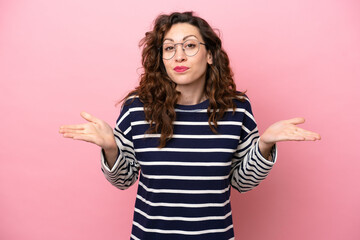 Wall Mural - Young caucasian woman isolated on pink background having doubts while raising hands