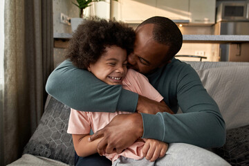 Wall Mural - Father embracing joyful little son on sofa at home