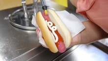 A Deliciously Fatty Hot Dog Is Cooked On A Street Cart. Mayonnaise Is Applied By Woman