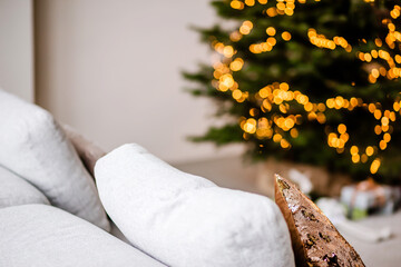 Wall Mural - Close up of pillow on sofa on background of Christmas tree with beautiful Christmas decorations in modern stylish interior. Magic Christmas background.