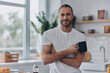 Handsome young man holding coffee cup and looking at camera while standing at the kitchen