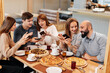 © Andrii - A group of friends is having pizza in a cozy restaurant and taking selfies, taking pictures together. A cheerful group of friends.
