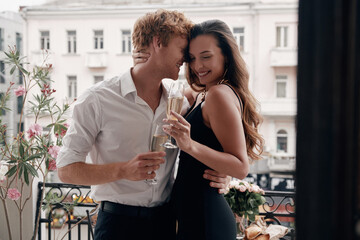 Beautiful well-dressed couple embracing while enjoying champagne on the balcony together