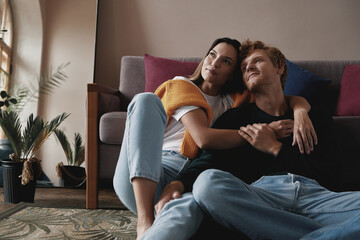 Sticker - Thoughtful young couple embracing and smiling while relaxing at home together