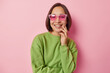 © wayhome.studio  - Portrait of cheeful Asian millennial girl smiles toothily dressed in casual green pullover and fashionable sunglasses being in good mood poses indoors against pink background. Positive emotions