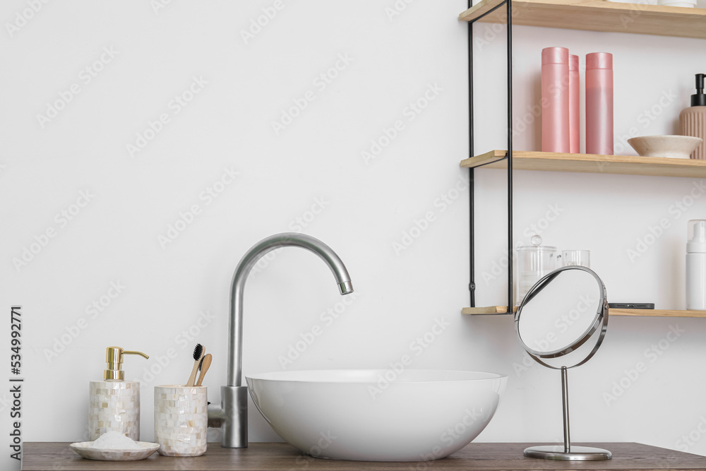 Modern sink and bath accessories on table near white wall