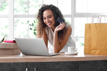 Young African-American woman with credit card and laptop shopping online at home