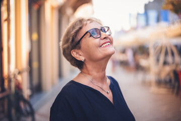 Portrait of happy active senior woman in glasses with a beautiful smile in profile walking in city on the street