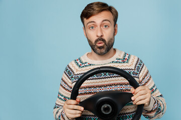 Young shocked surprised caucasian man 30s he wearing sweater hold steering wheel driving car look camera isolated on plain pastel light blue cyan background studio portrait. People lifestyle concept.