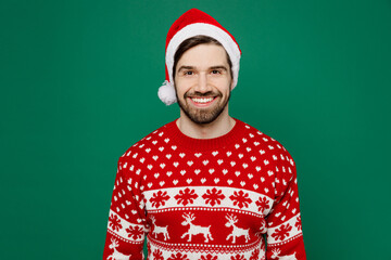 Wall Mural - Merry smiling happy cheerful young man 20s wear red warm knitted sweater Santa hat posing look camera isolated on plain dark green background studio portrait New Year 2023 holiday celebration concept