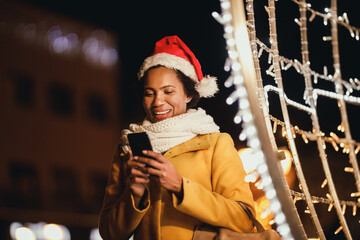 Wall Mural - Black Woman Using Smartphone In The City At Christmas Time