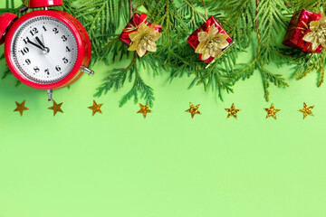 Wall Mural - Alarm clock  with tree branches and red gift boxes on green paper background. 5 minutes before the New Year. Creative greeting card.