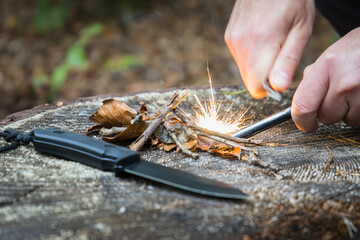 Wall Mural - Men with knife using a magnesium fire steel to start a fire in the woods