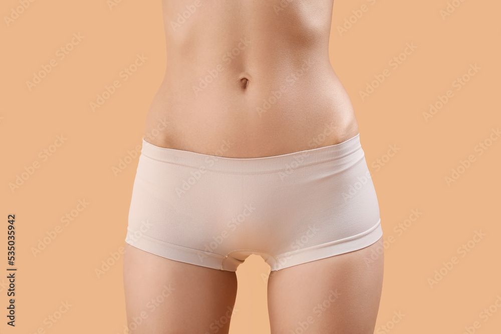 Slim young woman in underwear on beige background