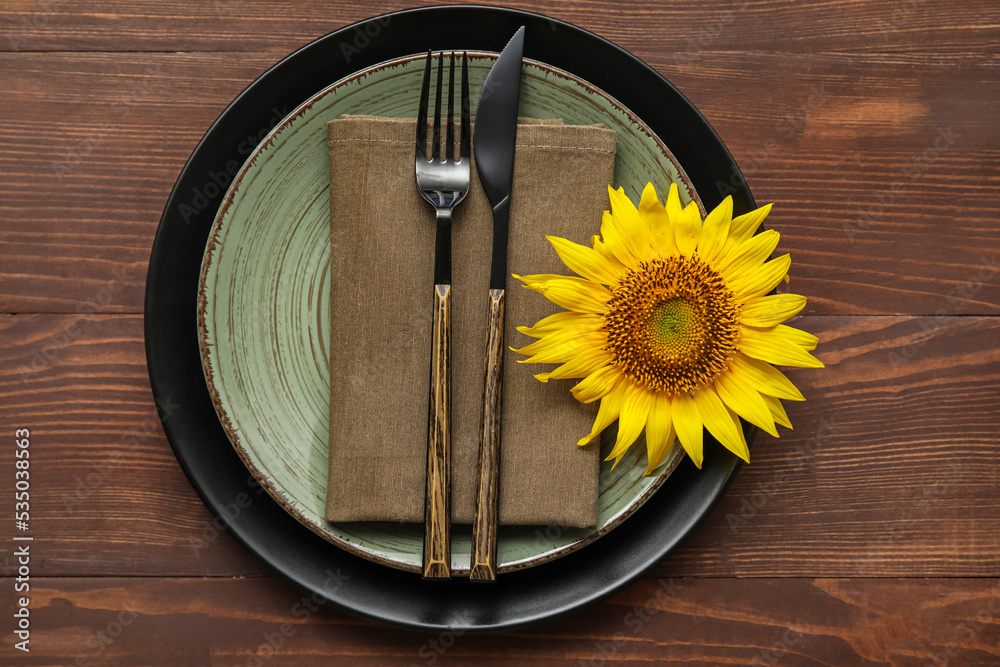 Table setting with stylish cutlery and sunflower on wooden background